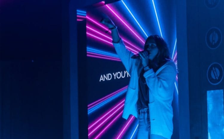 Singer performing on stage with neon lights.